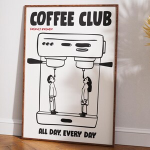 Op de afbeelding: Een ingelijste kunstprint met een koffiethema. De zwart-wit illustratie toont een koffiemachine met twee figuren eronder, die koffie drinken. De woorden "COFFEE CLUB" en "ALL DAY, EVERY DAY" staan op de poster.