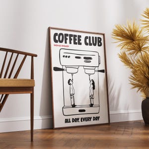 Op de afbeelding: Een ingelijste poster met de woorden "COFFEE CLUB" in een vetgedrukte letter, met "FRESHLY BREWED" eronder. De poster toont een zwart-wit illustratie van een koffiemachine met twee mensen die ernaar kijken. De tekst "ALL DAY, EVERY DAY" staat onderaan.