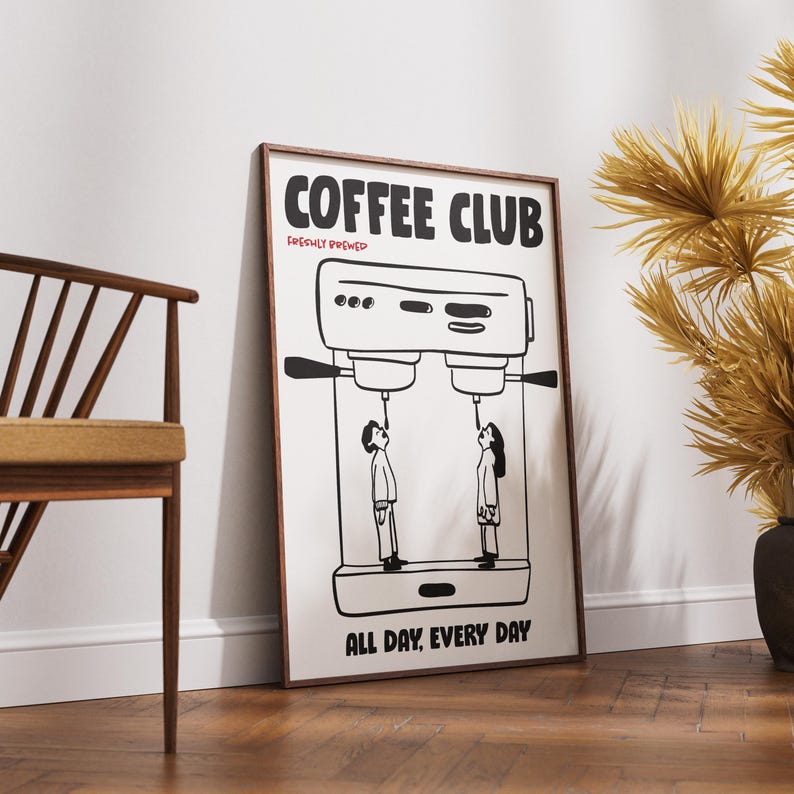 Op de afbeelding: Een ingelijste poster met de woorden "COFFEE CLUB" in een vetgedrukte letter, met "FRESHLY BREWED" eronder. De poster toont een zwart-wit illustratie van een koffiemachine met twee mensen die ernaar kijken. De tekst "ALL DAY, EVERY DAY" staat onderaan.