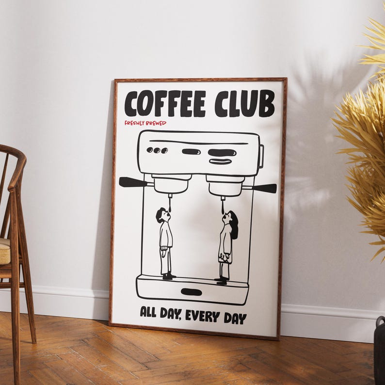 Op de afbeelding: Een ingelijste kunstprint met een koffiethema. De zwart-wit illustratie toont een koffiemachine met twee figuren eronder, die koffie drinken. De woorden "COFFEE CLUB" en "ALL DAY, EVERY DAY" staan op de poster.