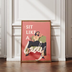 May include: A framed art print with a retro design. The print features a woman in a yellow top and black pants, seated in a green chair, with the words "SIT LIKE A LADY" in white script on a pink background.