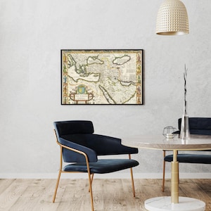 May include: Framed vintage map of the Ottoman Empire, featuring detailed cartography with historical illustrations and text. The map is in a black frame, displayed on a white wall. The room includes a blue chair and a round table.