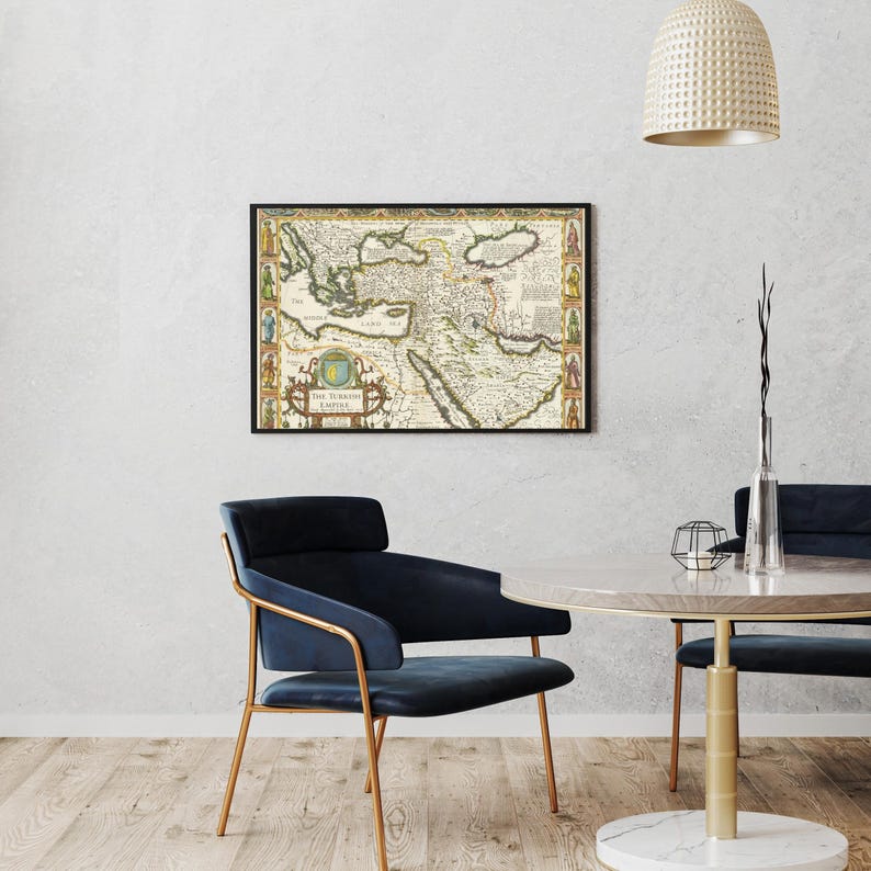 May include: Framed vintage map of the Ottoman Empire, featuring detailed cartography with historical illustrations and text. The map is in a black frame, displayed on a white wall. The room includes a blue chair and a round table.