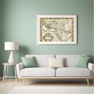 May include: A framed antique map of the Ottoman Empire, featuring detailed cartography and decorative borders. The map is displayed above a white sofa with green and cream-colored pillows. The room has a light green wall and a white lamp.
