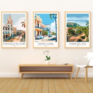 May include: Three colorful vintage travel posters featuring scenes from Cuba. The posters are framed in wood and feature the cities of Santiago de Cuba, Santa Clara, and Pinar del Rio.