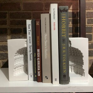 May include: A shelf arrangement featuring a collection of books, including "The Hobbit" by J.R.R. Tolkien, and bookends with a white architectural design. The books are in various colors and sizes, creating a visually appealing display.