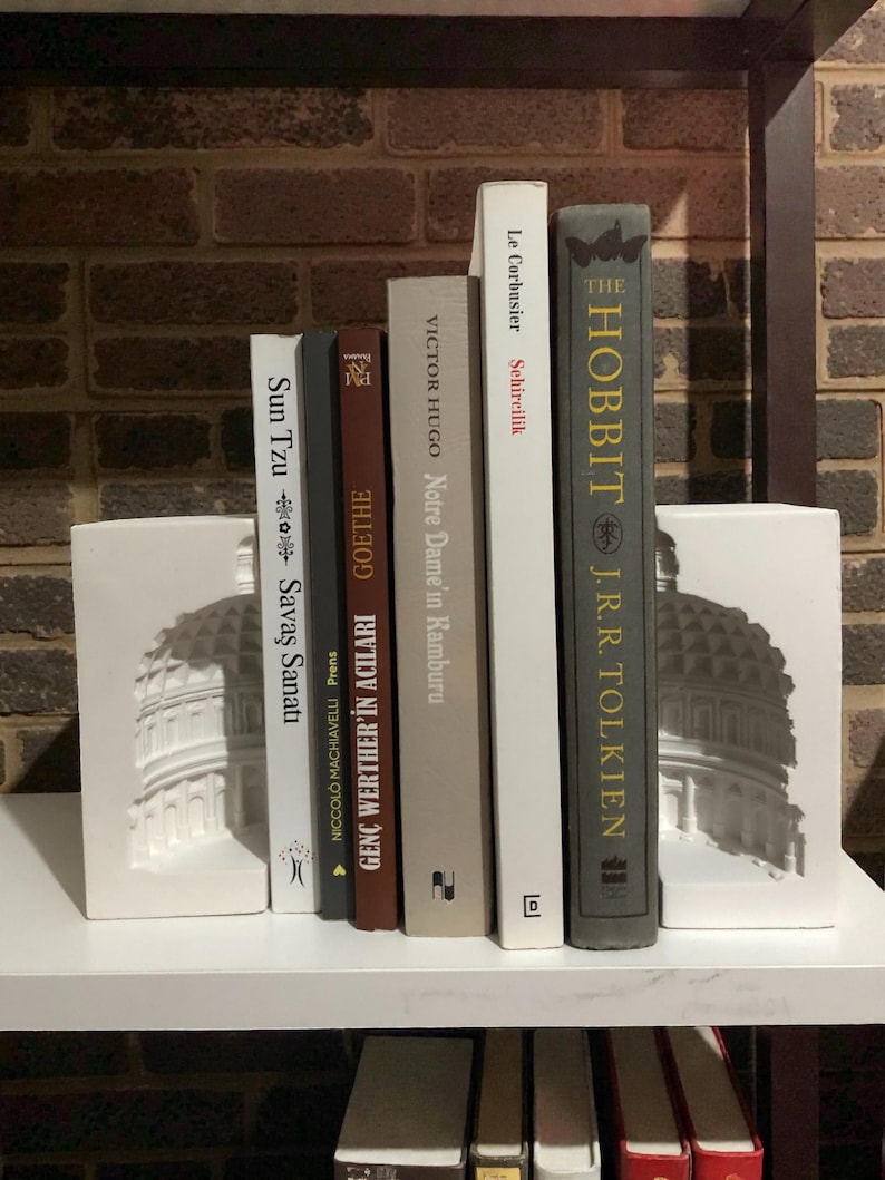 May include: A shelf arrangement featuring a collection of books, including "The Hobbit" by J.R.R. Tolkien, and bookends with a white architectural design. The books are in various colors and sizes, creating a visually appealing display.