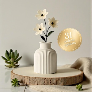 May include: A white ceramic vase with vertical ridges holds three white flowers with black centers. The vase sits on a wooden slice, with a small succulent and the text "31 colors options" in a gold circle.