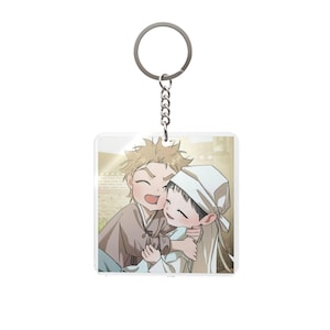 May include: A clear, square keychain featuring a cartoon illustration of two smiling figures embracing. The figures are dressed in traditional clothing, with one wearing a white hat. The keychain has a silver metal ring and chain.