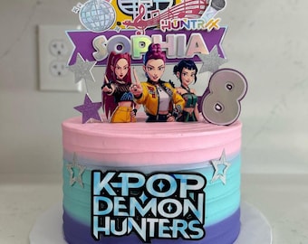 May include: A round, multi-layered cake with a gradient of pink, blue, and purple frosting. The cake is decorated with a K-Pop theme, featuring a topper with three animated figures, the name "Sophia", and the number "8". The words "K-Pop Demon Hunters" are also displayed.