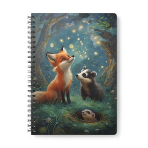 May include: Spiral-bound notebook featuring an illustration of a fox, badger, and hedgehog gazing upwards at glowing orbs in a forest setting. The fox has orange fur and the badger has black and white fur. The hedgehog peeks out from a burrow.