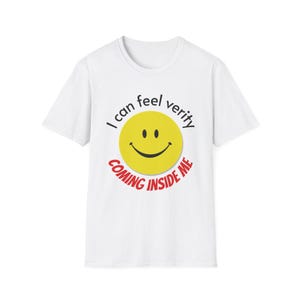 Puede incluir: Una camiseta blanca de manga corta con un gráfico central de una cara sonriente amarilla. Sobre la cara, el texto negro dice I can feel verity, y debajo de la cara, el texto rojo dice COMING INSIDE ME en una fuente negrita y mayúscula.