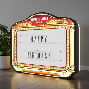 May include: A marquee-style light box with the words "HAPPY BIRTHDAY" displayed. The sign has a black frame with gold and red accents, and the top reads "BUFFALO BILLS". The light box is illuminated.