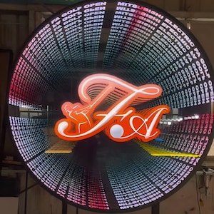 May include: A circular infinity mirror sign featuring a bright orange neon-style logo of a golfer swinging a club with the letters FA. The surrounding frame displays repeating text that reads MITSUBISHI ELECTRIC FA GOLF OPEN in white.