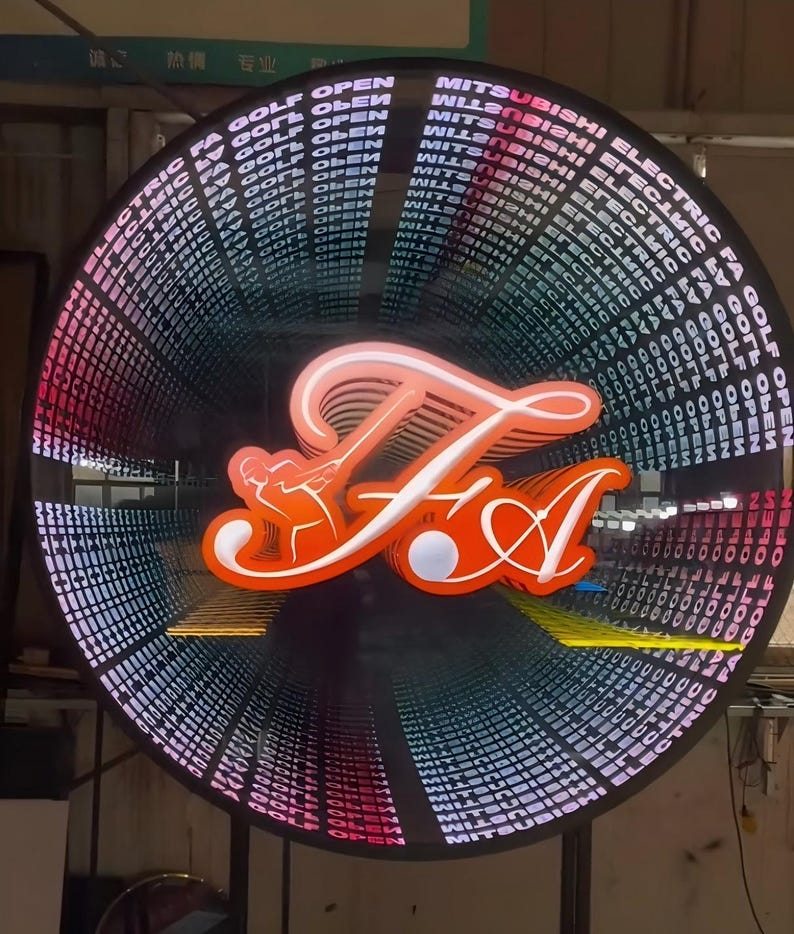 May include: A circular infinity mirror sign featuring a bright orange neon-style logo of a golfer swinging a club with the letters FA. The surrounding frame displays repeating text that reads MITSUBISHI ELECTRIC FA GOLF OPEN in white.