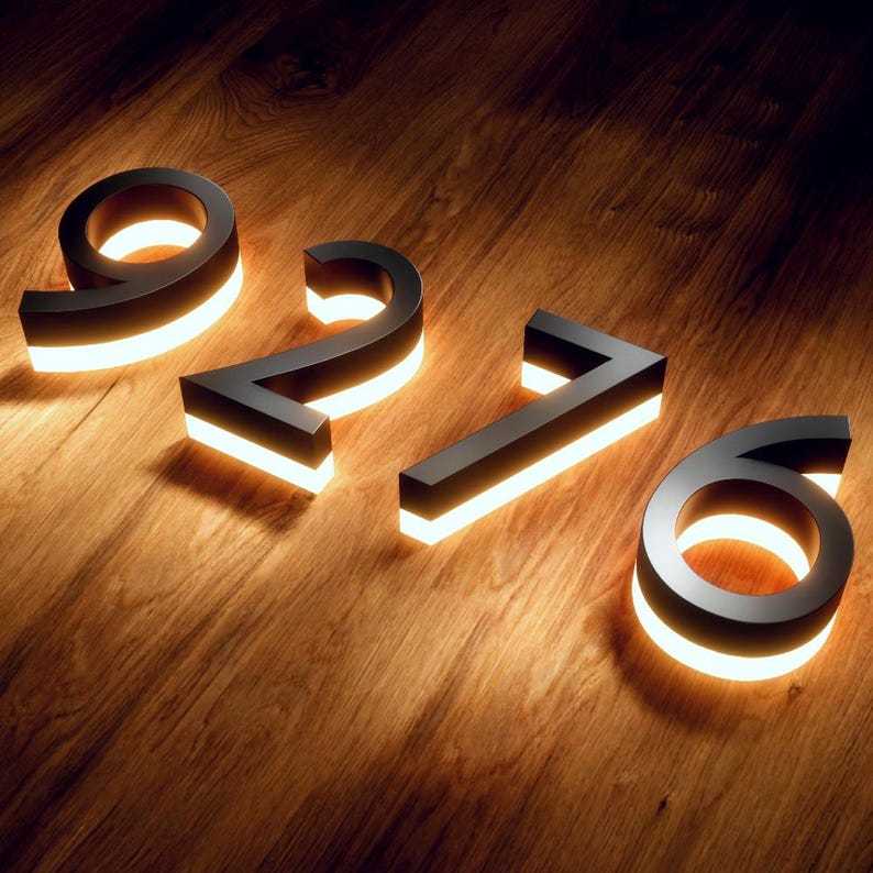 May include: Black metal illuminated house numbers 9276, with a warm white glow. The numbers are displayed on a wooden surface, creating a modern and elegant aesthetic. The numbers are approximately 6 inches tall.
