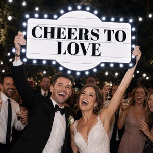 May include: A rectangular marquee-style sign with rounded edges and a black frame featuring a border of small, illuminated white LED bulbs. The white center panel displays the black text CHEERS TO LOVE in a bold, sans-serif capital font.
