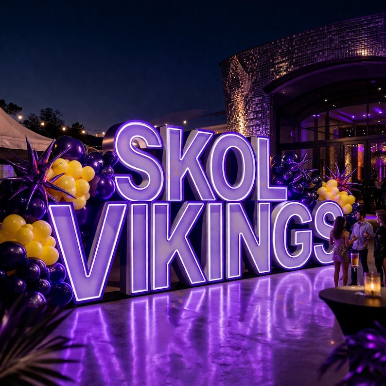 May include: Large illuminated sign that reads "SKOL VIKINGS" in purple and white. The sign is surrounded by purple and yellow balloons and decorative starbursts. The scene is set outdoors at night, with a building in the background.