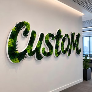 May include: A large, wall-mounted sign featuring the word Custom in a cursive script font. The letters are outlined in white and filled with a variety of preserved green mosses and dark green fern leaves, creating a textured, three-dimensional effect.