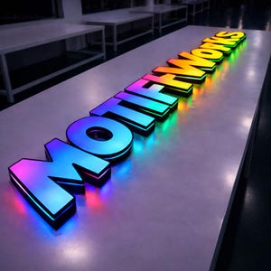 Pode incluir: Letreiro iluminado com a inscri&ccedil;&atilde;o "MOTIF WORKS" em letras grandes e tridimensionais. As letras s&atilde;o iluminadas com um gradiente de cores, que vai do azul ao verde e ao amarelo. O letreiro est&aacute; colocado sobre uma superf&iacute;cie clara.