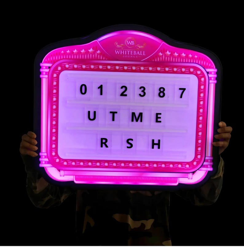 May include: A pink illuminated sign with the text "WHITEBALL LOUNGE" at the top. The sign has a grid with the numbers 0, 1, 2, 3, 8, and 7, along with the letters U, T, M, E, R, S, and H. The sign is held up against a black background.