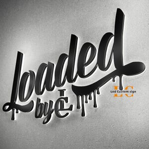 May include: A black 3D wall sign featuring the stylized text "loaded by LC" with a dripping paint effect. The letters have a glossy finish and are illuminated from behind with a white LED glow. The text "Led Custom sign" appears in orange.