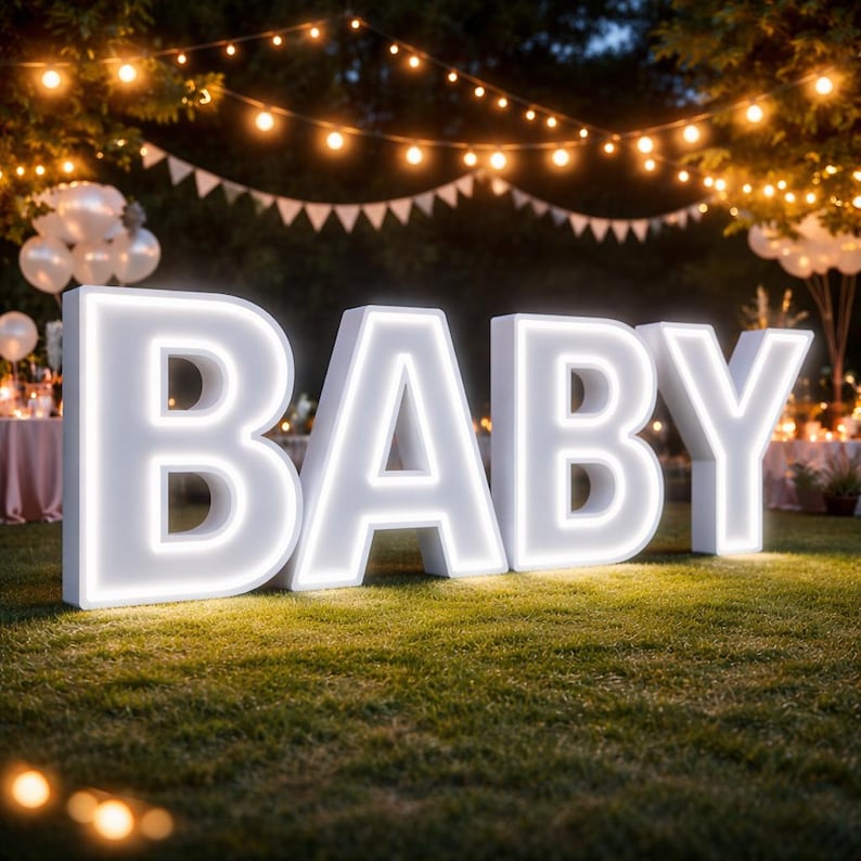 May include: Large, illuminated white letters spell out the word "BABY" on a grassy lawn. The letters have a bright, glowing outline. The scene is decorated with string lights and a festive atmosphere, suggesting a baby shower or gender reveal party.