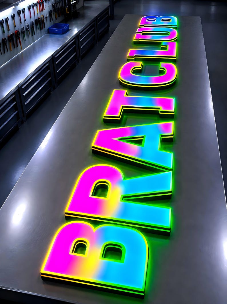 Puede incluir: Un letrero luminoso con la inscripci&oacute;n "BRAT CLUB". Las letras son grandes y multicolores, con una transici&oacute;n de rosa a amarillo a azul, delineadas en negro y verde. El letrero est&aacute; sobre una superficie met&aacute;lica.