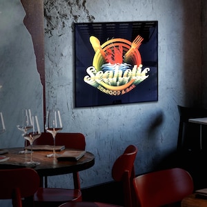 May include: A square wall sign featuring a dark background with a central graphic of a red lobster, a yellow spoon, and a yellow fork. The text reads Seaholic in a stylized white font, with the words SEAFOOD & BAR printed in smaller yellow letters below.