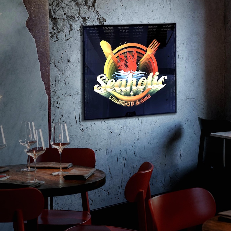 May include: A square wall sign featuring a dark background with a central graphic of a red lobster, a yellow spoon, and a yellow fork. The text reads Seaholic in a stylized white font, with the words SEAFOOD & BAR printed in smaller yellow letters below.