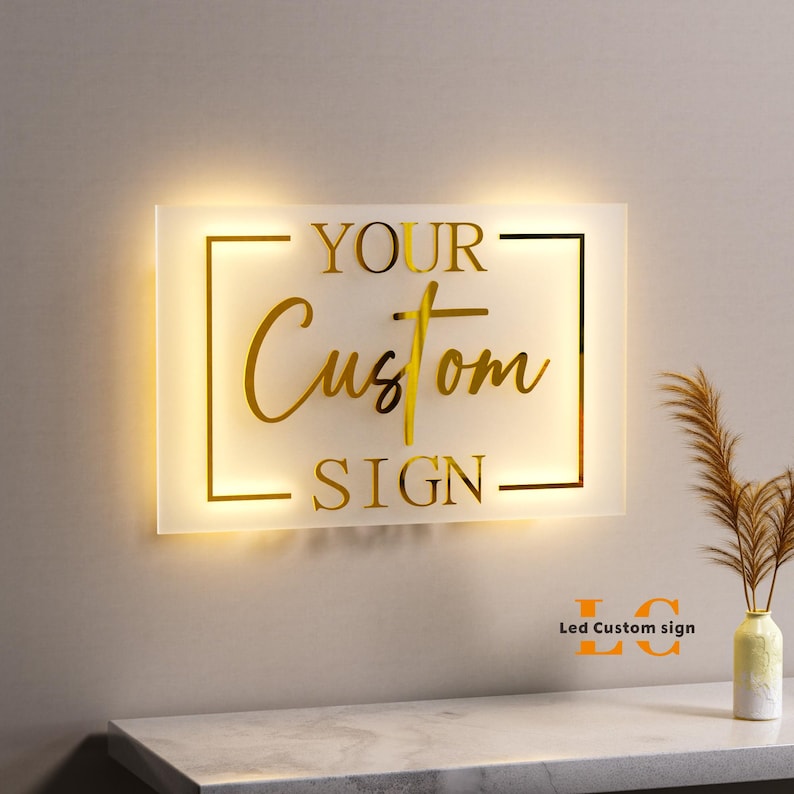 May include: A rectangular, illuminated sign with the words "YOUR Custom SIGN" in gold lettering. The sign is lit from behind, creating a warm glow. The words are inside a gold rectangular frame. The sign is mounted on a wall.