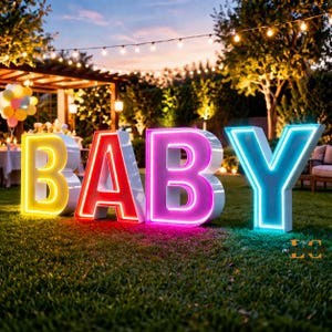 May include: Large, illuminated letters spelling "BABY" are displayed on a grassy lawn. The letters are white with colorful neon outlines: yellow, red, pink, and blue. The scene is set outdoors with string lights and trees.