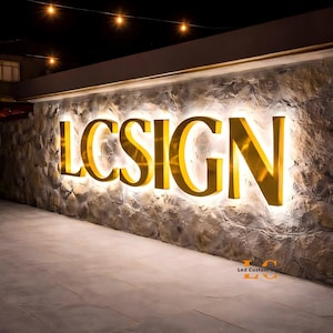 May include: A large, illuminated wall sign featuring the gold-colored, three-dimensional letters spelling LCSIGN. The letters are mounted on a textured, light-gray stone wall and emit a bright, warm white glow from behind each character.