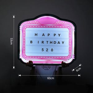 May include: A pink and black light-up sign with the words "HAPPY BIRTHDAY 520". The sign is 23.6 inches wide, 20.9 inches tall, and 2.4 inches thick. The sign has a retro theater marquee design.