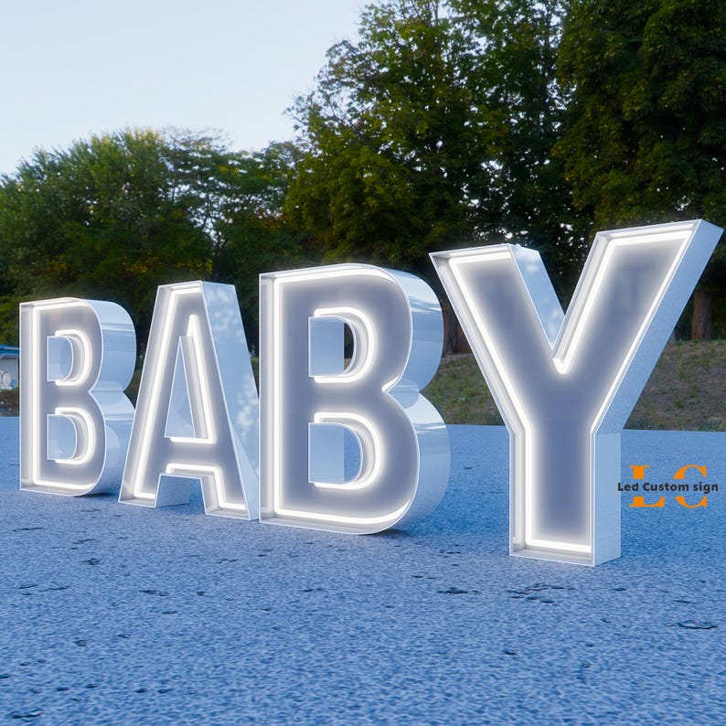 K&ouml;nnte beinhalten: Gro&szlig;es, beleuchtetes "BABY"-Schild mit wei&szlig;em Finish und hellem, leuchtendem Umriss. Das Schild steht auf einer strukturierten Oberfl&auml;che, im Hintergrund B&auml;ume. Der Text "Led Custom sign" ist unten rechts sichtbar.