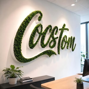 May include: A large, three-dimensional wall sign featuring the word Custom written in a cursive script. The letters are constructed with white edges and filled with dense, vibrant green preserved moss, creating a textured, natural appearance.