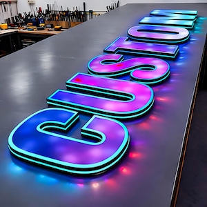 Pode incluir: Letreiro luminoso com a palavra "CUSTOM" em letras grandes e tridimensionais. As letras transitam do azul para o roxo com uma contorno preto e um brilho de n&eacute;on. O letreiro est&aacute; sobre uma superf&iacute;cie cinza.