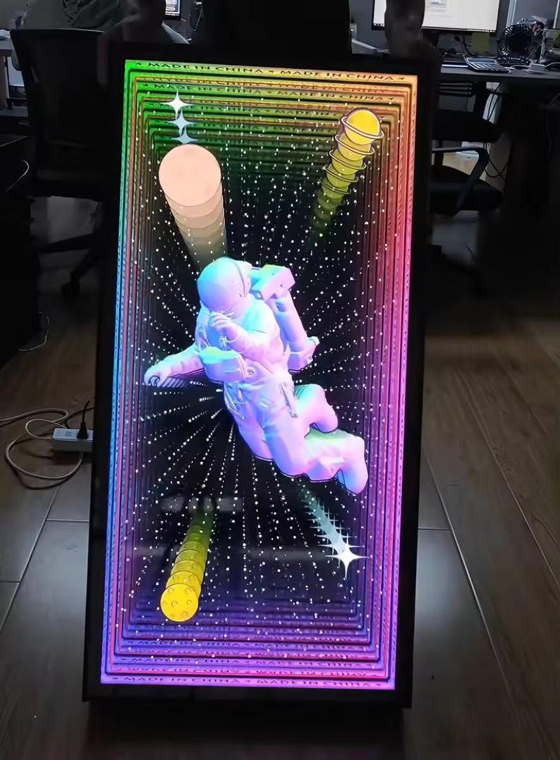 May include: A rectangular infinity mirror featuring a central white astronaut figure floating against a deep black background with a multi-colored rainbow light border. The design includes yellow planet icons and white star shapes, with the text MADE IN CHINA.