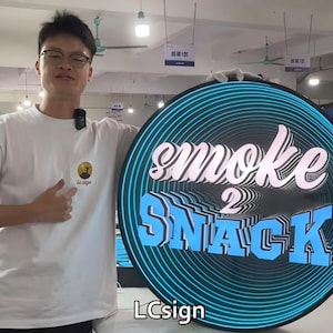 May include: A round sign with the words "smoke 2 SNACK" in white and blue, with a blue neon outline. The sign is held by a person wearing a white t-shirt. The sign also has the text "LCsign".