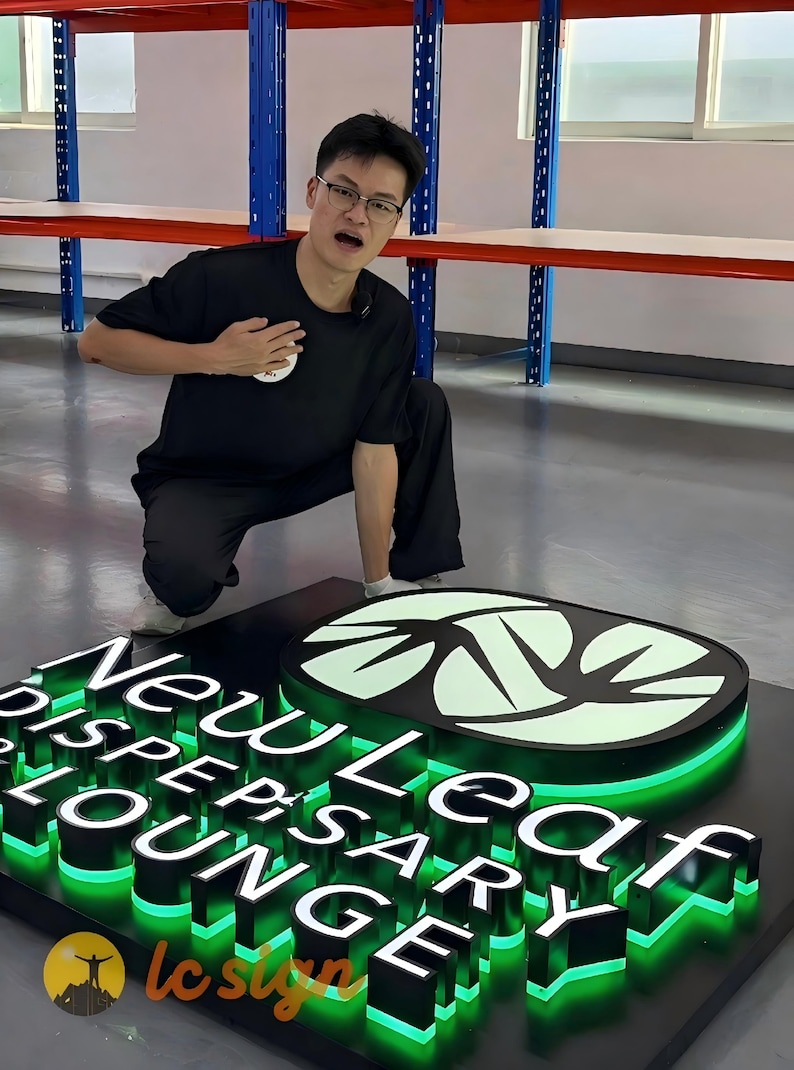 Pu&ograve; includere: Un'insegna luminosa tridimensionale personalizzata con il testo New Leaf Dispensary Lounge in lettere nere in rilievo. L'insegna include un logo a foglia verde brillante e una retroilluminazione a LED verde su una base rettangolare nera.