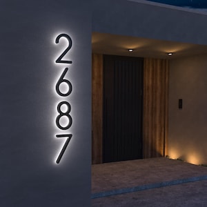 May include: Illuminated house number 2687 in a modern font, mounted on a dark gray wall. The numbers are black with a bright white glow around them. The design is sleek and contemporary.