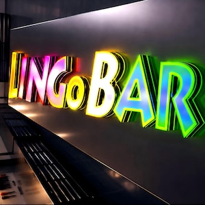 Puede incluir: Letrero luminoso que dice "LINGO BAR" en letras 3D coloridas. Las letras est&aacute;n delineadas en negro y tienen un degradado de colores, incluyendo rosa, amarillo y azul. El letrero est&aacute; montado en una pared gris oscura.