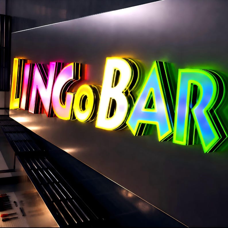 Puede incluir: Letrero luminoso que dice "LINGO BAR" en letras 3D coloridas. Las letras est&aacute;n delineadas en negro y tienen un degradado de colores, incluyendo rosa, amarillo y azul. El letrero est&aacute; montado en una pared gris oscura.