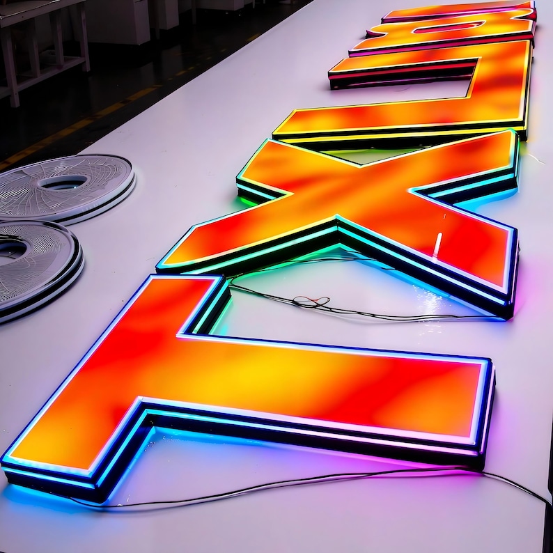 Pode incluir: Letras laranja e amarelas iluminadas que soletram "FX" com um efeito gradiente. As letras t&ecirc;m uma borda preta e s&atilde;o contornadas com luzes LED azuis, verdes e rosa. As letras est&atilde;o em uma superf&iacute;cie branca.