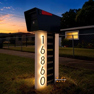 May include: A modern black mailbox with a red flag sits atop a white and black address post. The address numbers "16860" are illuminated in a warm glow. The sign is set in a grassy yard with a sunset backdrop.