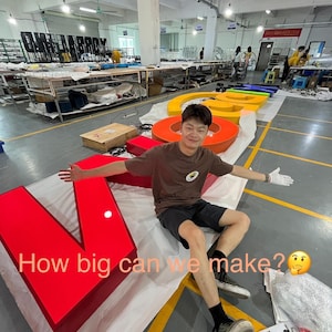 May include: A large, multi-colored, three-dimensional channel letter sign spelling out a word, featuring a bright red letter V in the foreground. The sign includes yellow, orange, and blue letters. Text on the image reads: How big can we make?