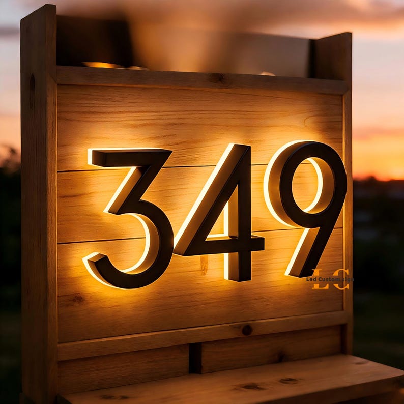 May include: Wooden address sign displaying the numbers 349 in a modern font. The numbers are illuminated with a warm, inviting glow, set against a backdrop of natural wood. The sign is mounted on a wooden structure, perfect for outdoor use.