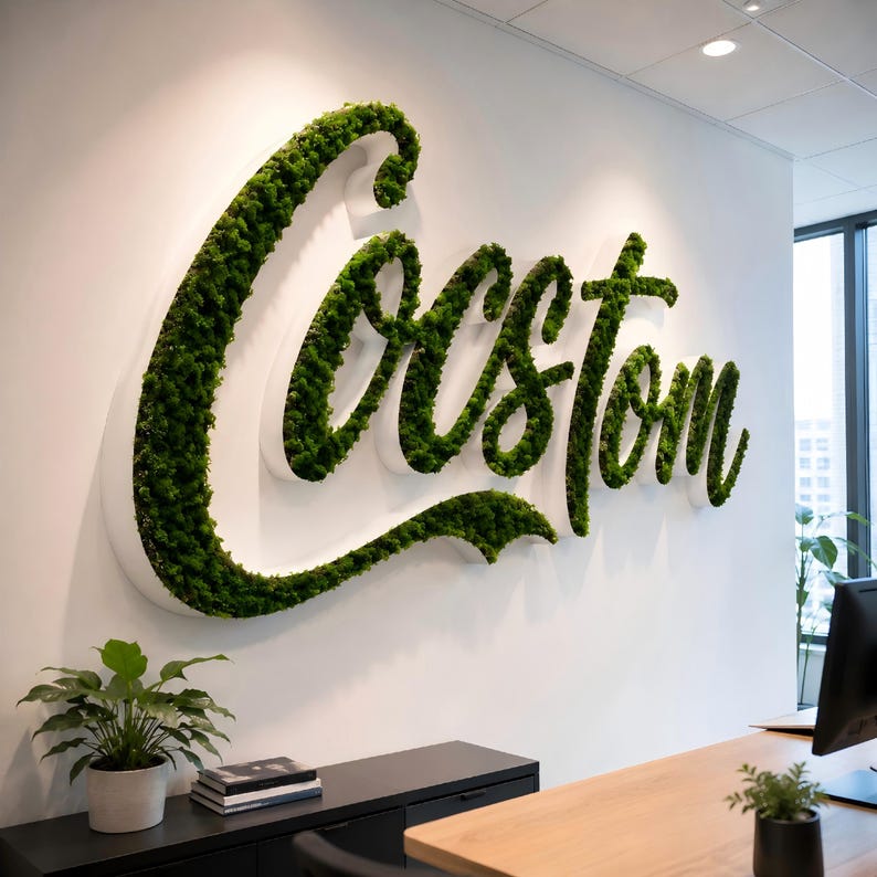May include: A large, three-dimensional wall sign featuring the word Custom in cursive script. The letters are constructed with white edges and filled with dense, vibrant green preserved moss, creating a textured, natural appearance on the wall.