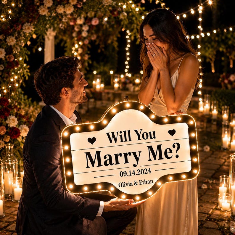 以下が含まれることがあります： Will You Marry Me?、日付14.09.2024、名前Olivia & Ethanの文字が入った、カスタムメイドのマーキー風ライトアップサイン。中央は白地で黒い文字が書かれ、ハートのアイコンと小さな電球で縁取られたデザイン。
