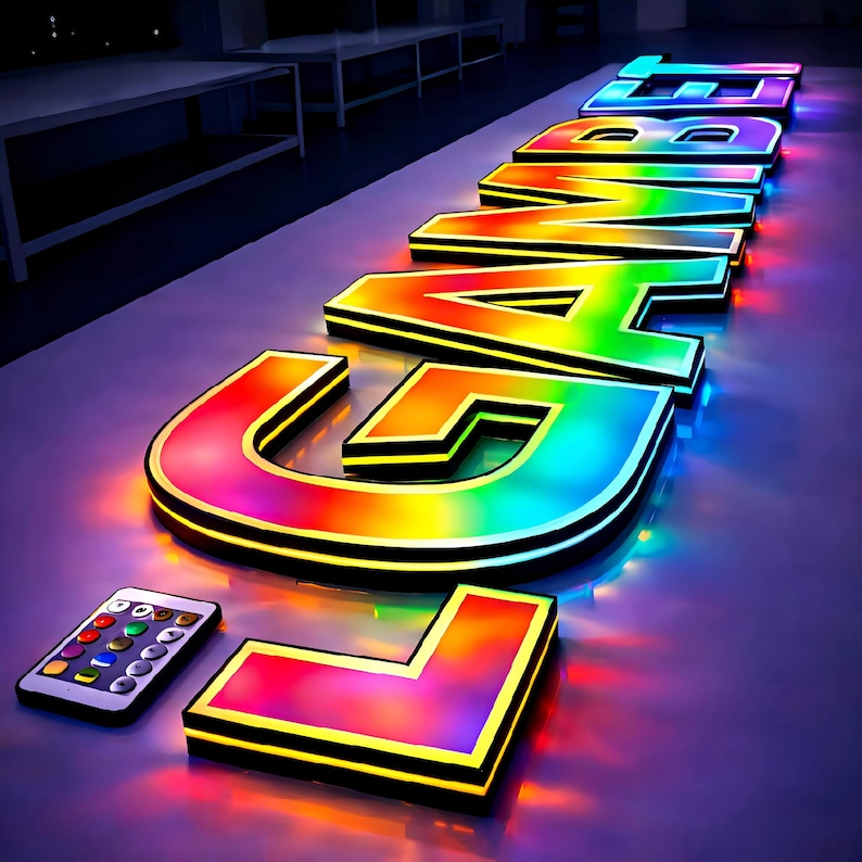 May include: Illuminated "GAME" sign with a rainbow gradient effect, outlined in black. A remote control with colored buttons sits beside the sign. The letters glow with vibrant colors, creating a dynamic and eye-catching display.
